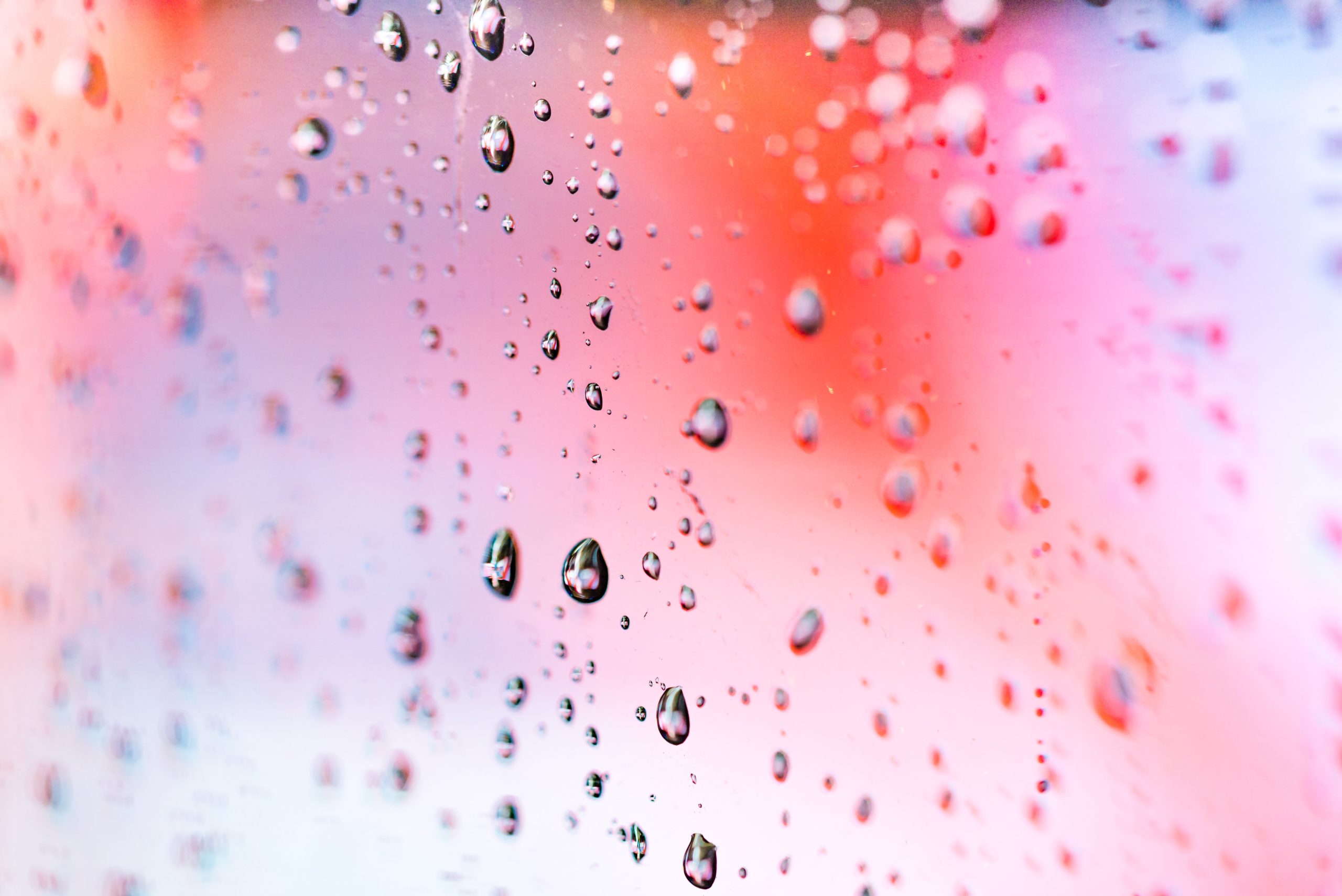 Raindrops rolling down a red, purple and pink reflective screen